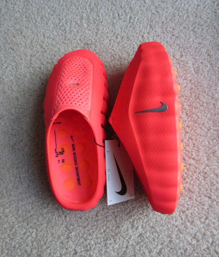 Red Nike shoes on a gray carpet with a white tag.