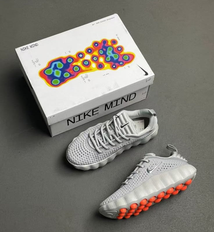Gray sneakers with orange soles next to a Nike Mind box on a gray background