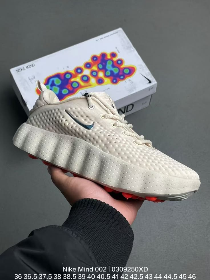 Beige sneaker held in hand with colorful box in the background