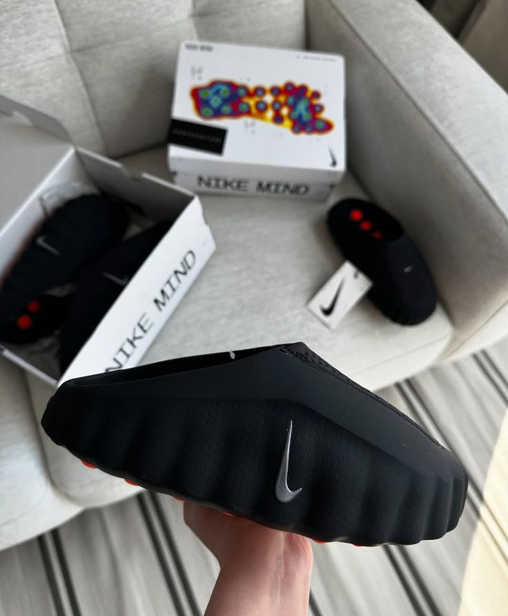 Black sneaker with Nike logo held over a box labeled 'Nike Mind' on a light gray surface.
