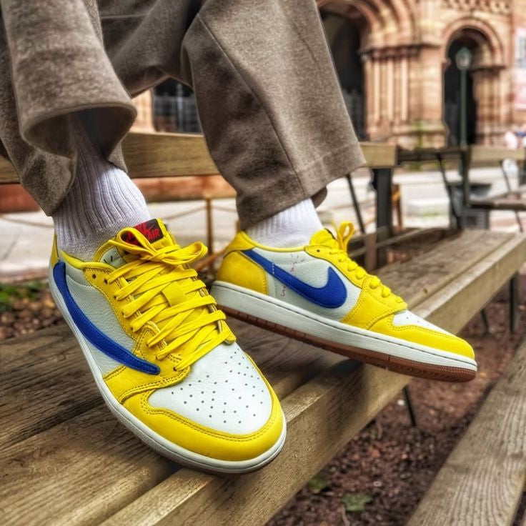 Yellow and blue sneakers with white soles worn by a person sitting on a wooden bench.