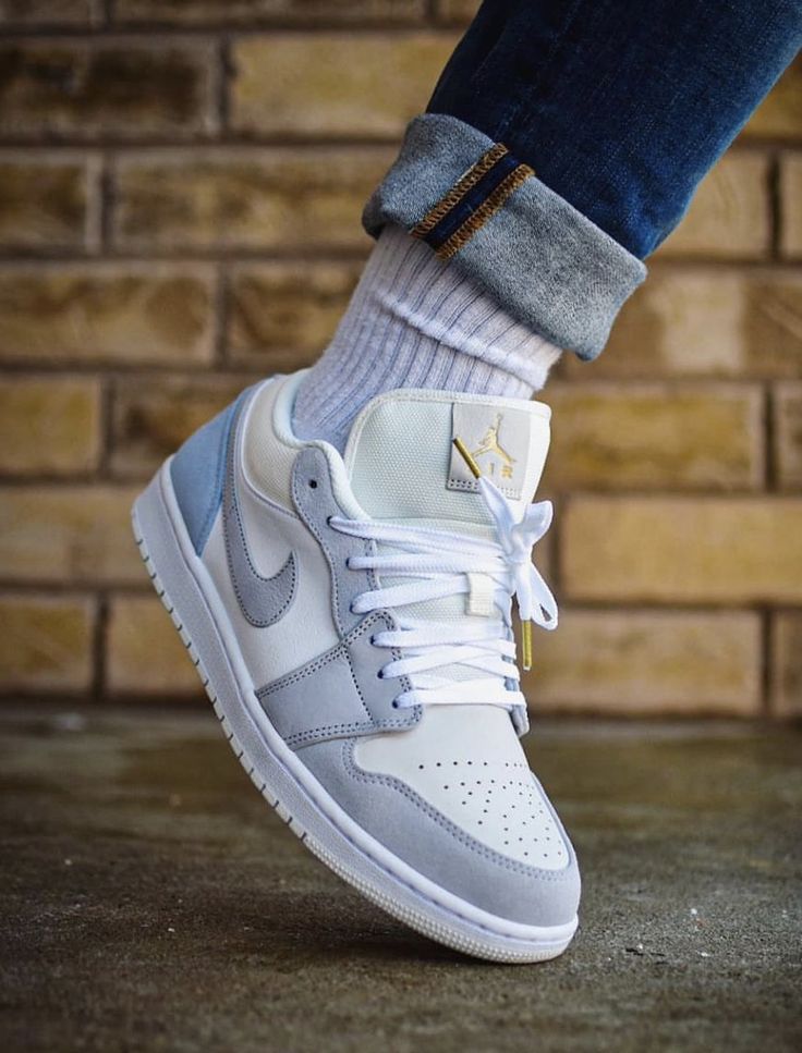 Gray and white sneaker with Nike logo worn by a person against a brick wall.